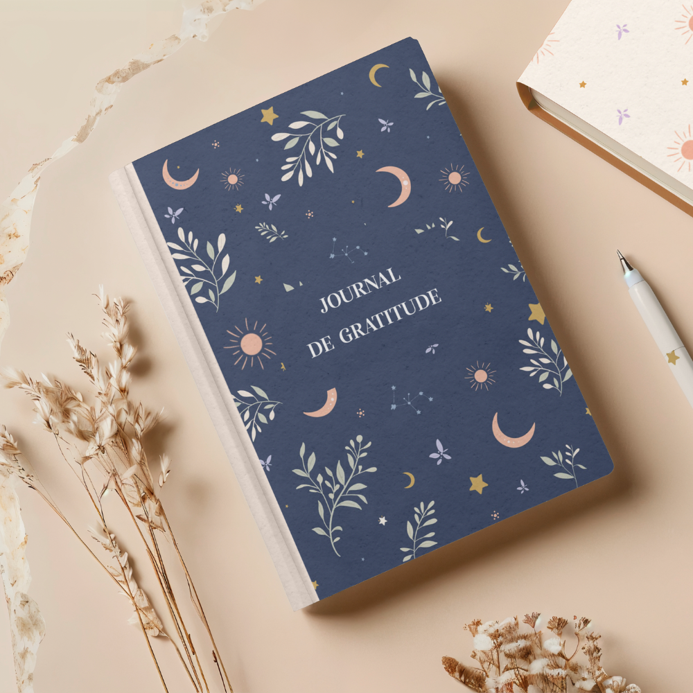 Journal de gratitude posé sur une table avec fleurs séchées, illustrant un design de motifs floraux pour packaging holistique et papeterie.